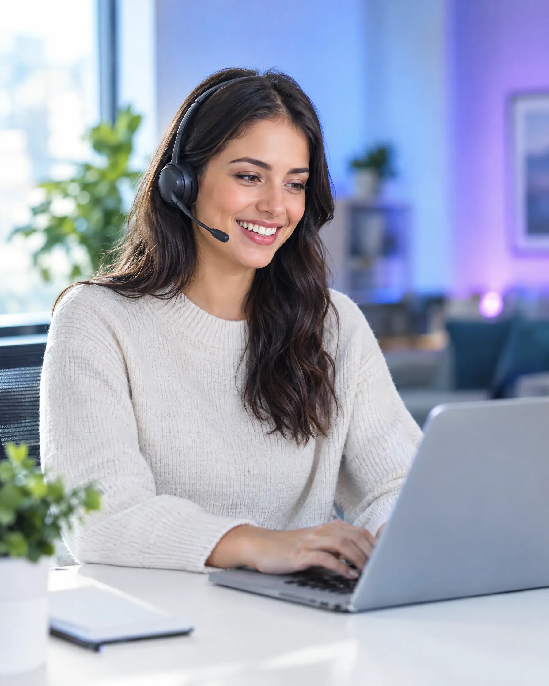 A smiling support agent with a headset answering chats on her laptop